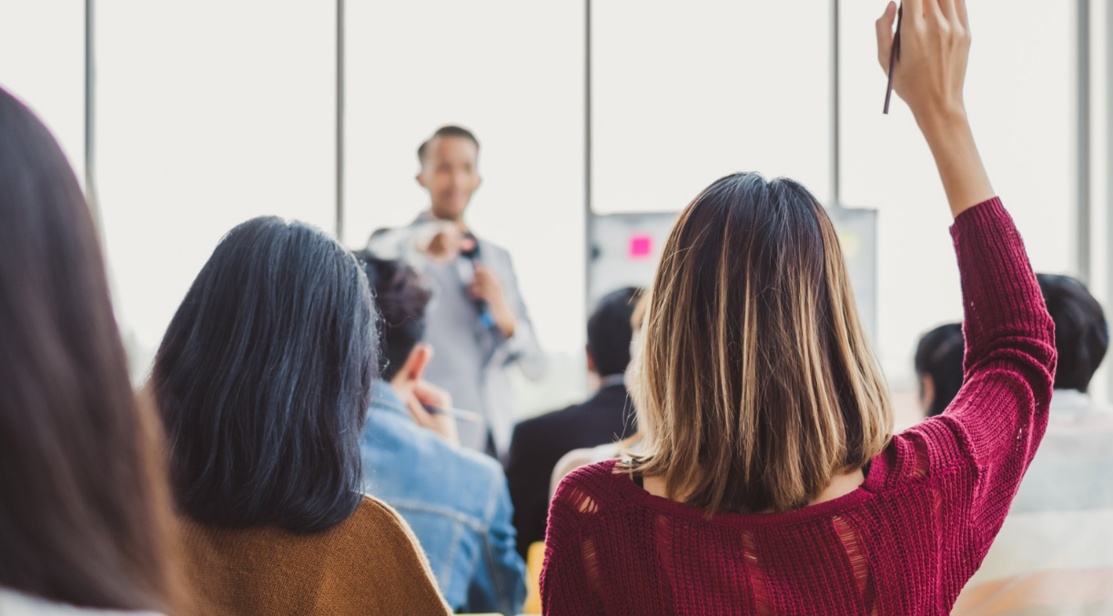 A woman is raising her hand in a classroom to answer a question.