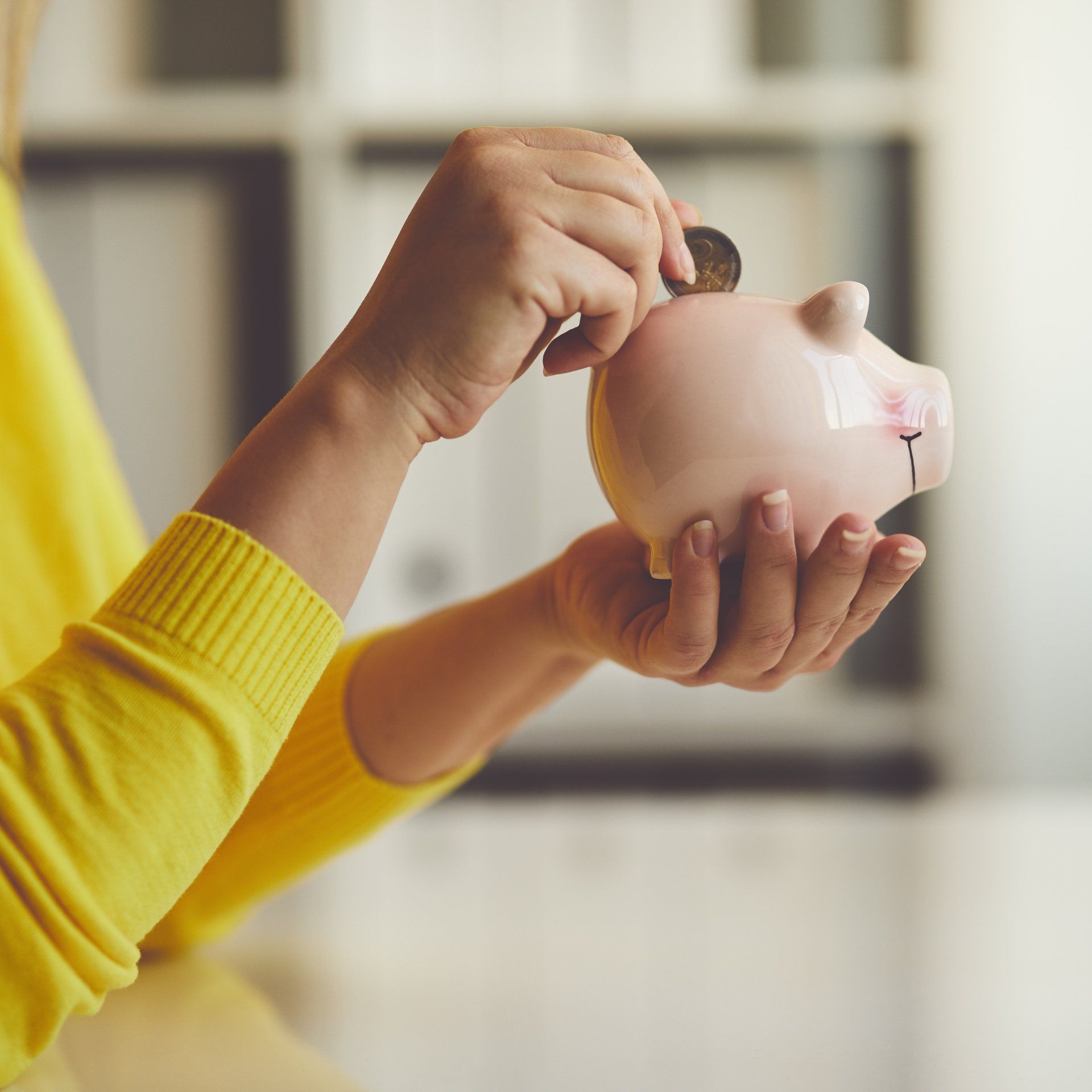 A woman is putting a coin into a piggy bank.
