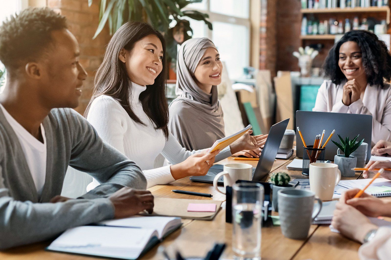 A group of people are sitting around a table with laptops.