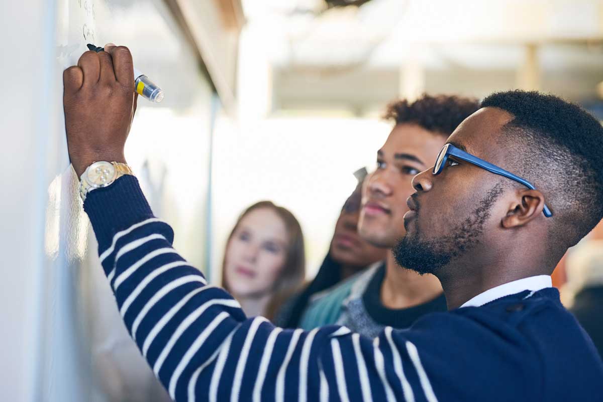 A man is writing on a whiteboard in front of a group of people.