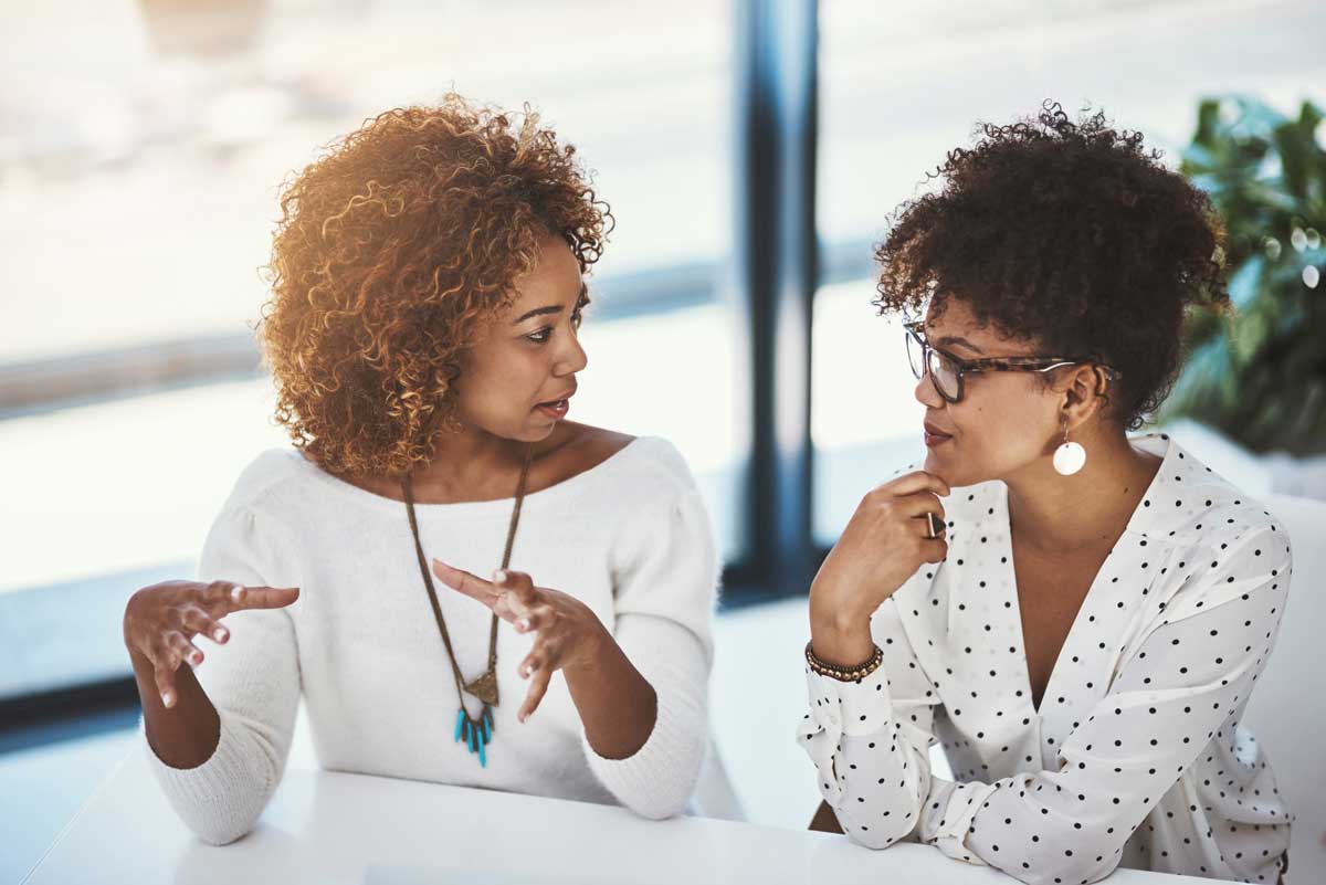 Two women are sitting at a table talking to each other.
