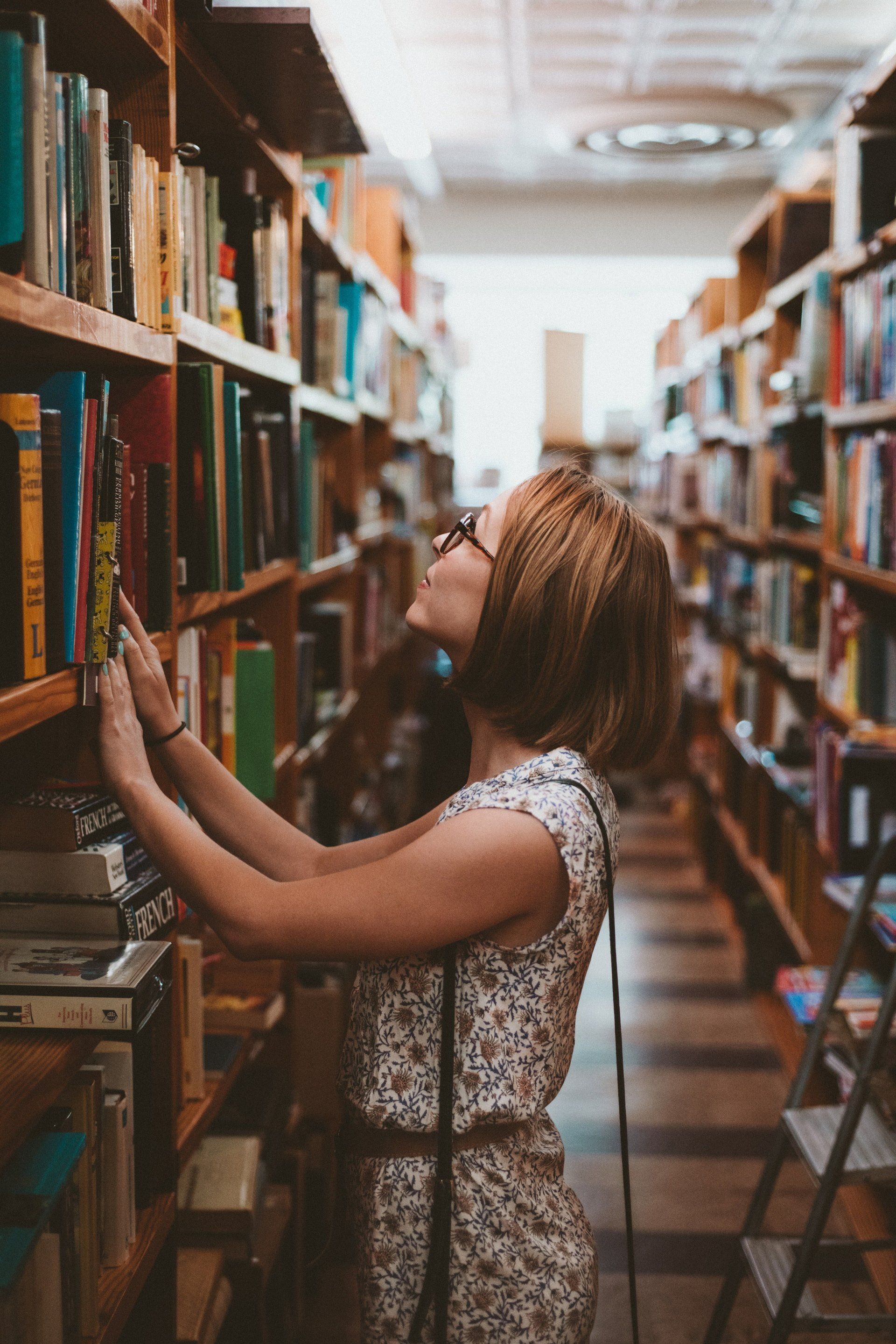 A woman is looking at books on a shelf in a library.