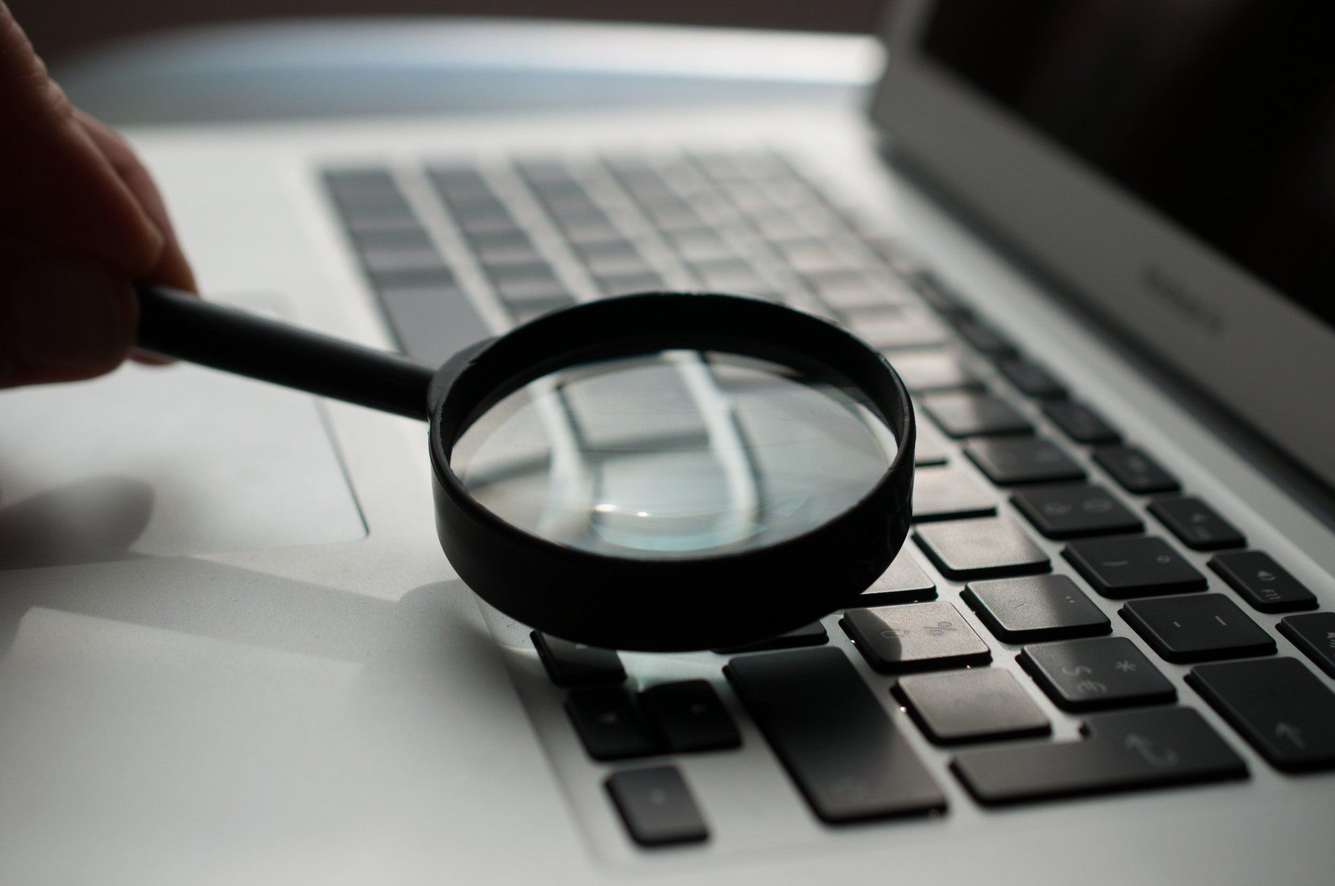 A person is holding a magnifying glass over a laptop keyboard.