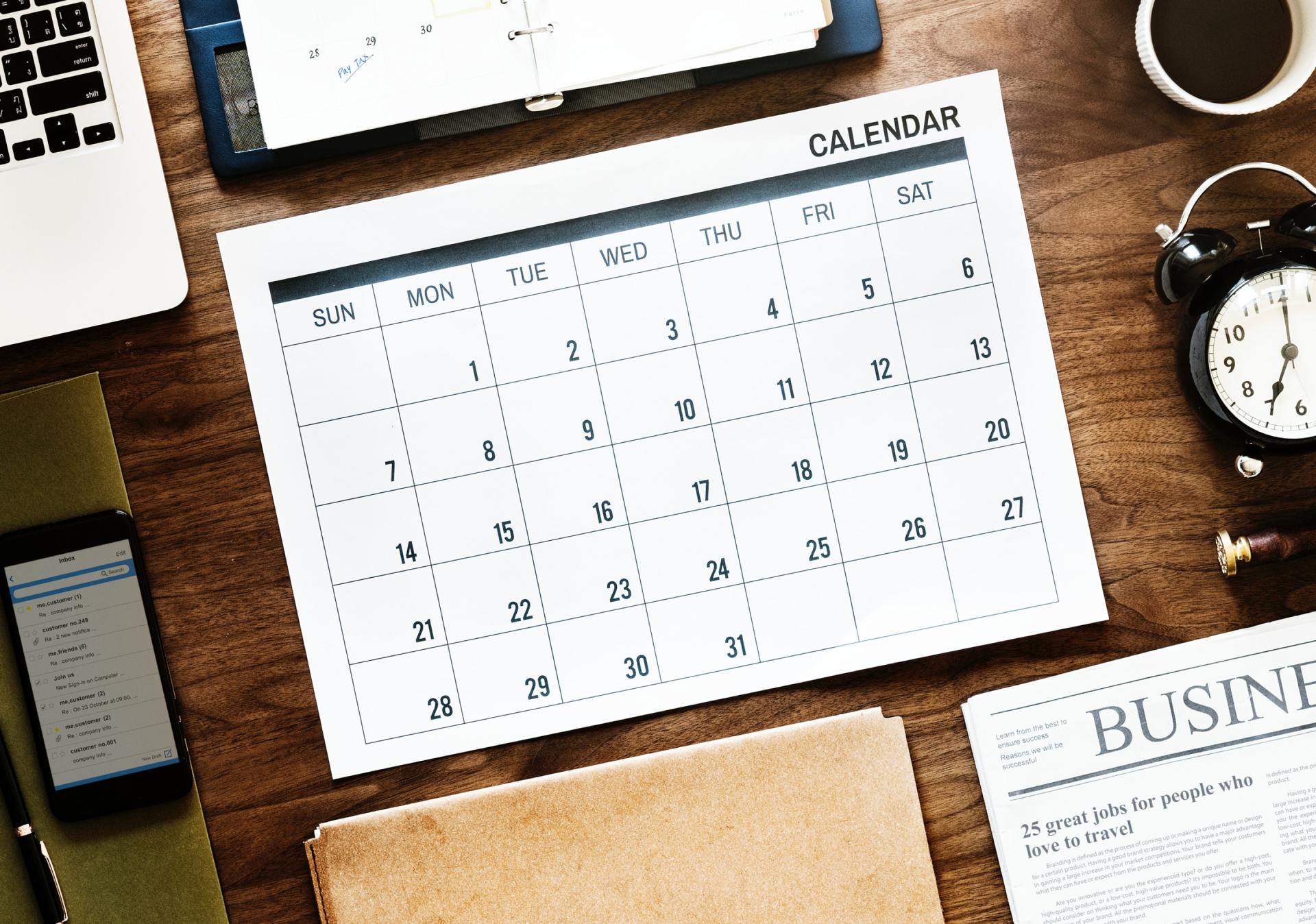 A calendar is sitting on top of a wooden table next to a laptop.